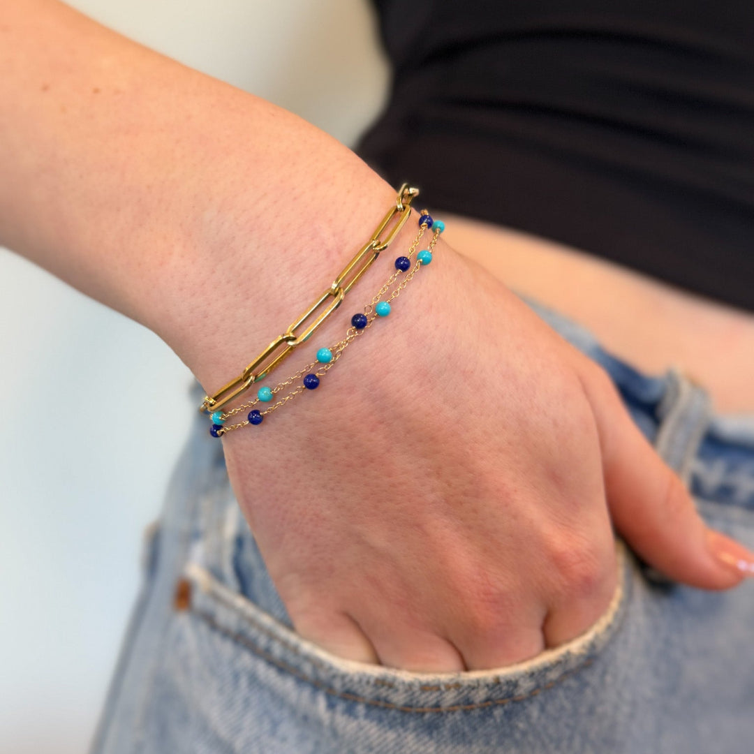 A person putting their hand in their pocket wearing a turquoise beaded bracelet, lapis beaded bracelet and a paperclip chain bracelet all in 14k gold.