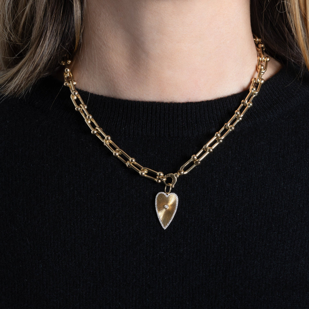 Gold chain necklace with a heart pendant worn by a person on a black background
