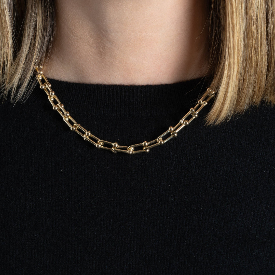 Gold chain necklace worn by a person with a black sweater on.