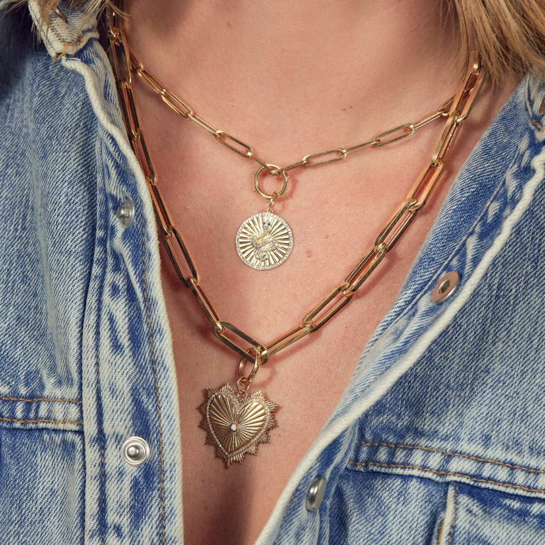 A person wearing gold paperclip chain necklaces with charms and a denim shirt.