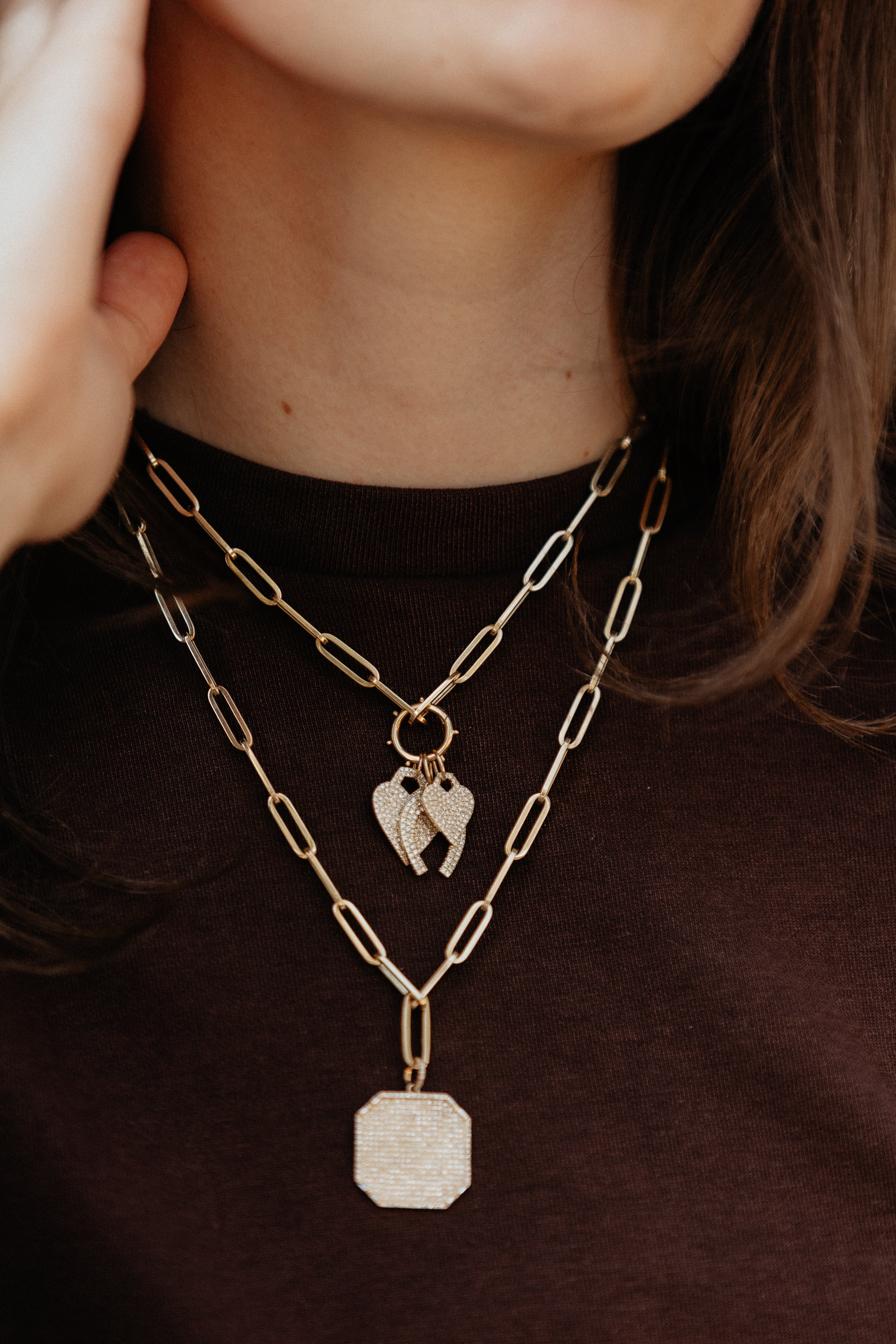 A person in a brown shirt with gold paperclip chains and pavé diamond pendants