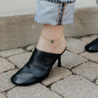 Two ankle bracelets worn with rolled-up jeans on a stone pavement.