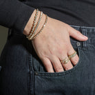 A person wearing three diamond tennis bracelets set in gold and two diamond rings set in gold. 