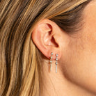 Close-up of an ear wearing a set of diamond earrings with blonde hair.