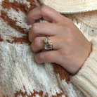 A close-up of a person's hand wearing a 14k yellow gold  bezel set moi et toi ring, resting on a cream and rust-khaki knit sweater.