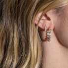 A person wearing one large hoop earrings featuring bezel set lab grown diamonds and one claw shaped huggie.