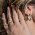 A person pulling their hair back, showcasing two earrings -  one large hoop earrings featuring bezel set lab grown diamonds and one claw shaped huggie. 