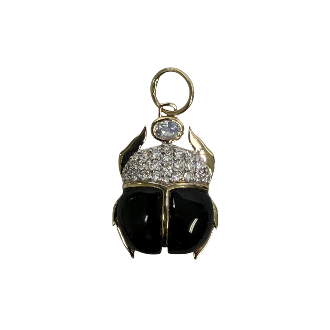 A 14k gold scarab pendant made with black onyx, diamond pavé and moonstone all set on a white background. 
