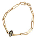 A 14k gold paperclip chain bracelet with a black enamel and emerald bead on a white background.