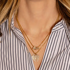 Two gold necklaces with beads and pendants on a person wearing a striped shirt