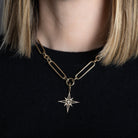 A person wearing a chunky link chain with a diamond pave starburst pendant. 