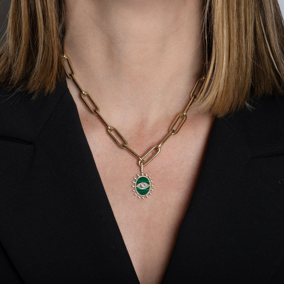 A person wearing a chunky 14k gold paperclip chain necklace with a malachite and diamond pendant attached. 
