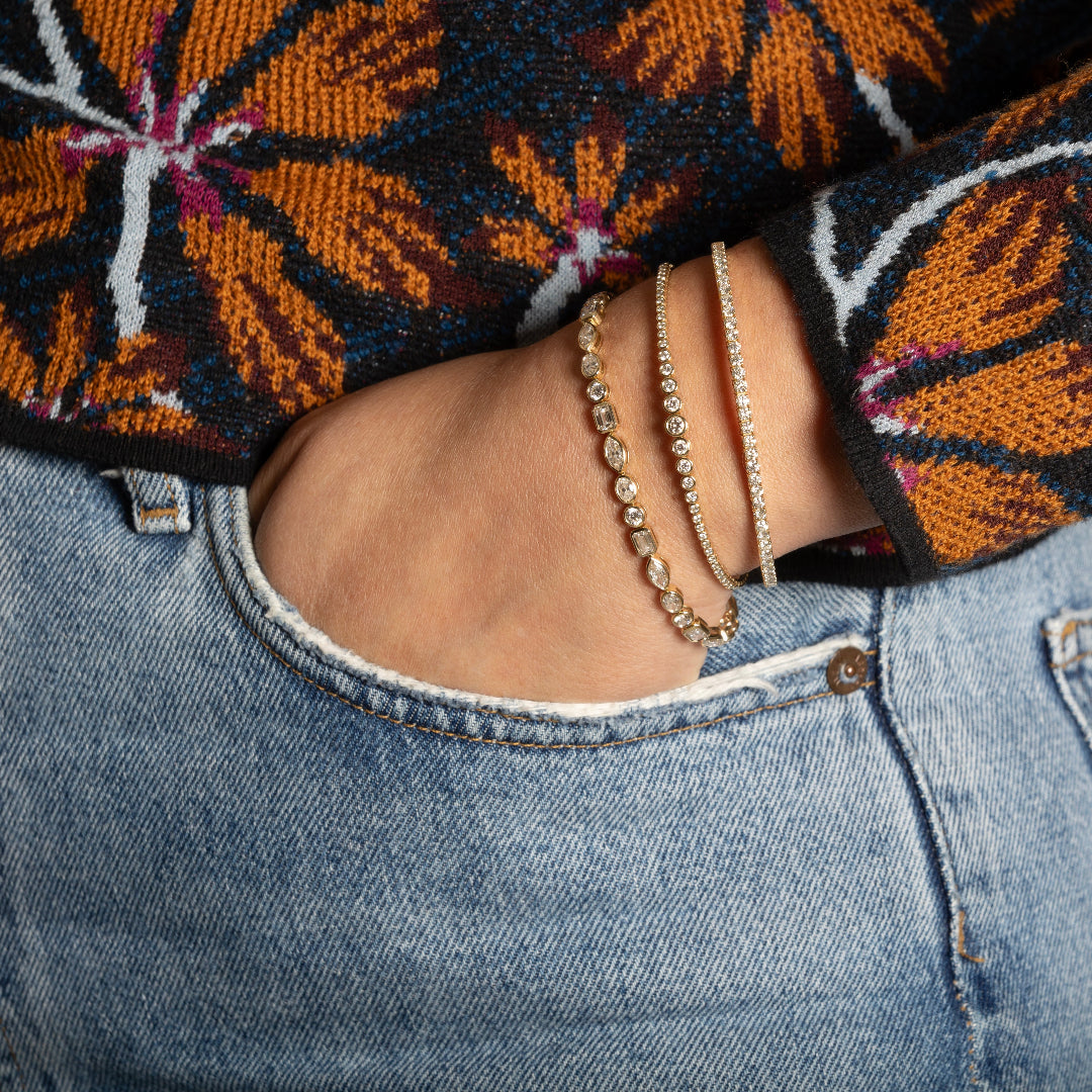 A person wearing three diamond bracelets with their hand in their pocket. 