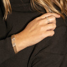 Close-up of a hand wearing multiple gold bracelets and a gold and diamond ring against a black shirt.