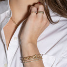 Close-up of a person wearing multiple gold bracelets and rings on a white shirt background
