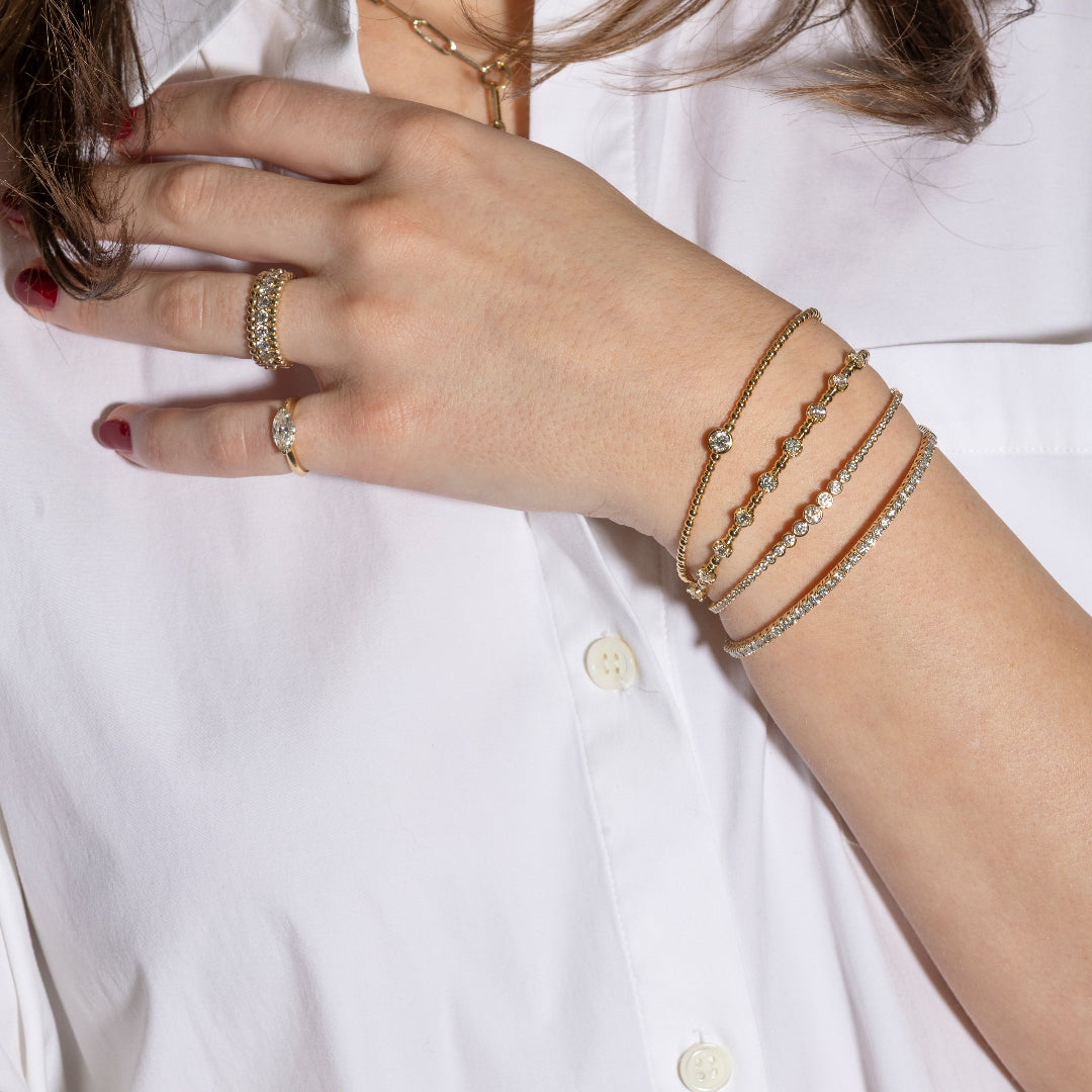 Close-up of a hand wearing multiple gold bracelets on a white shirt background