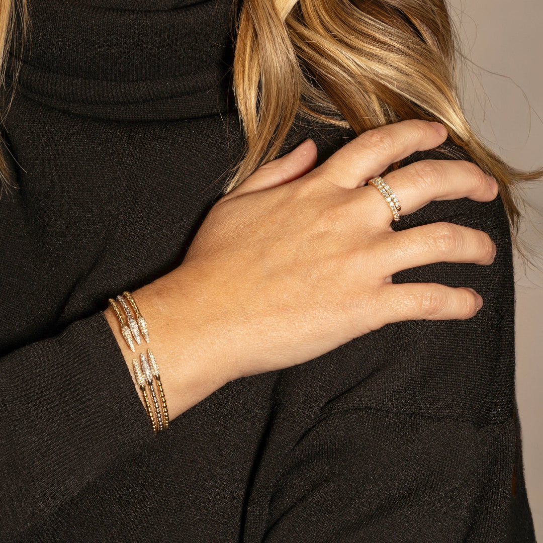 Close-up of a person wearing gold and white gold flexi bracelets and a ring and a black sweater