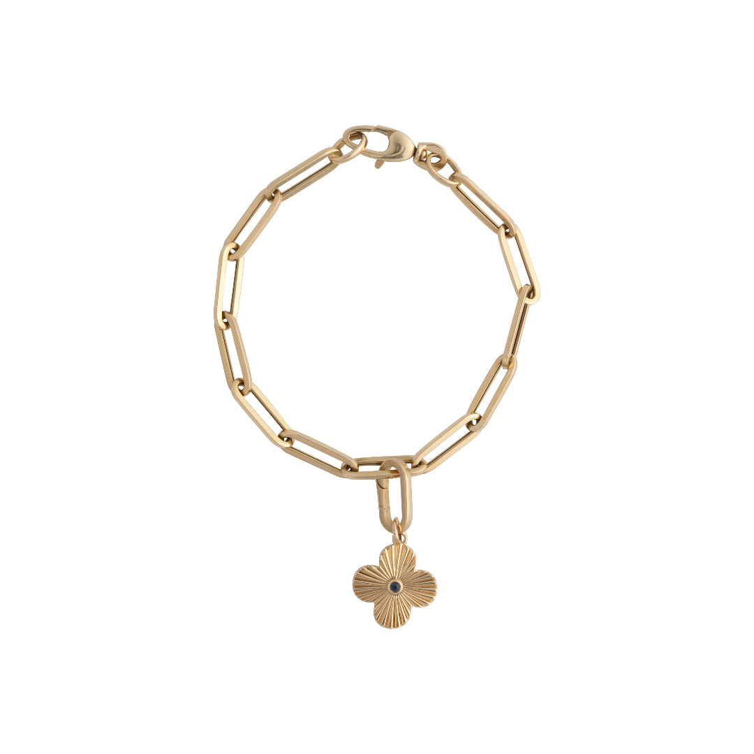 A 14k gold pendant featuring a blue sapphire center stone with clover-shaped rays around it attached to a paperclip chain bracelet. 