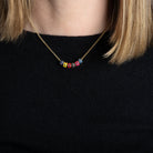 A person in a black sweater wearing a thin gold chain with colored enamel beads. 