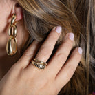 A person pulling their hair out of their face to showcase chunky gold earrings and two gold rings with confetti diamonds. 