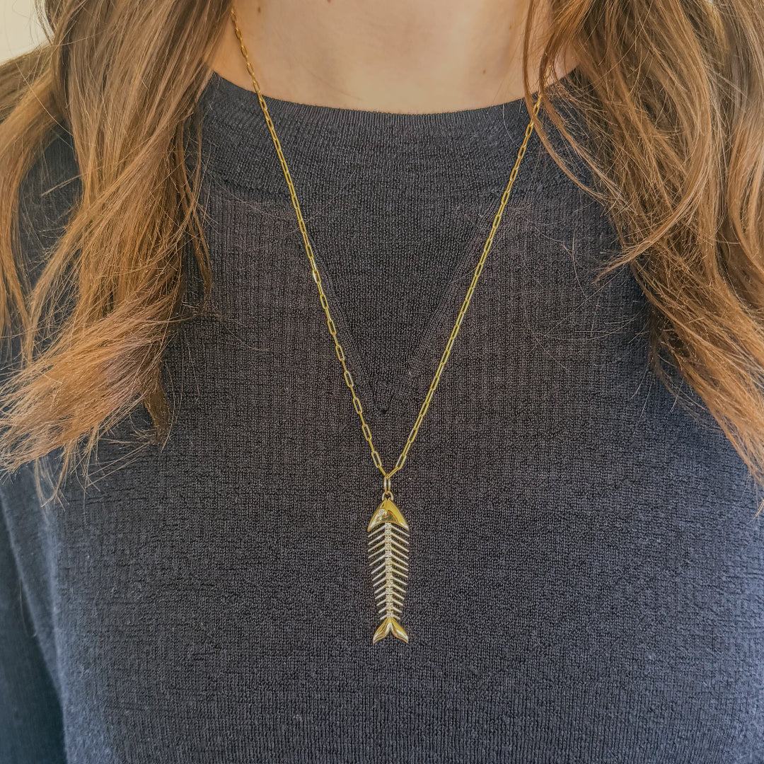 Person wearing a gold necklace with a gold and diamond fish pendant against a neutral background