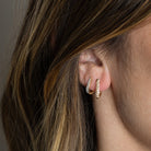 Someone wearing two of diamond pave huggie earrings.