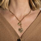 Gold necklace with heart-shaped pendant worn by a person in a brown sweater.