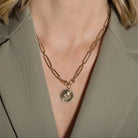 Gold chain necklace with a pendant worn by a person in a green blazer.