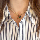 A person wearing a striped shirt and tennis necklace with pendants made of emerald, ruby and blue sapphire. 