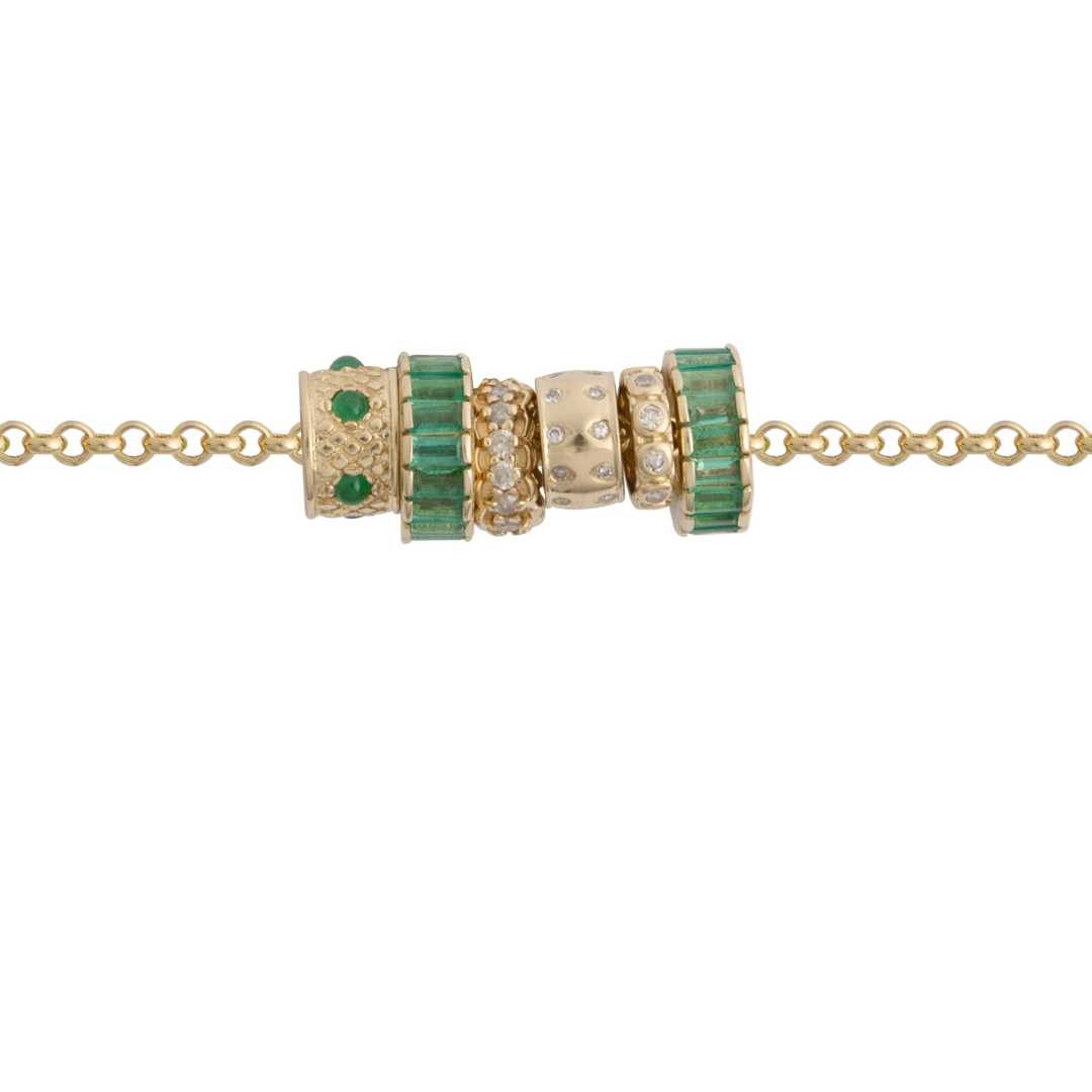 A gold chain with emerald and diamond beads on a white background. 