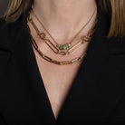 Close-up of a person wearing gold necklaces with emerald beads against a black background.
