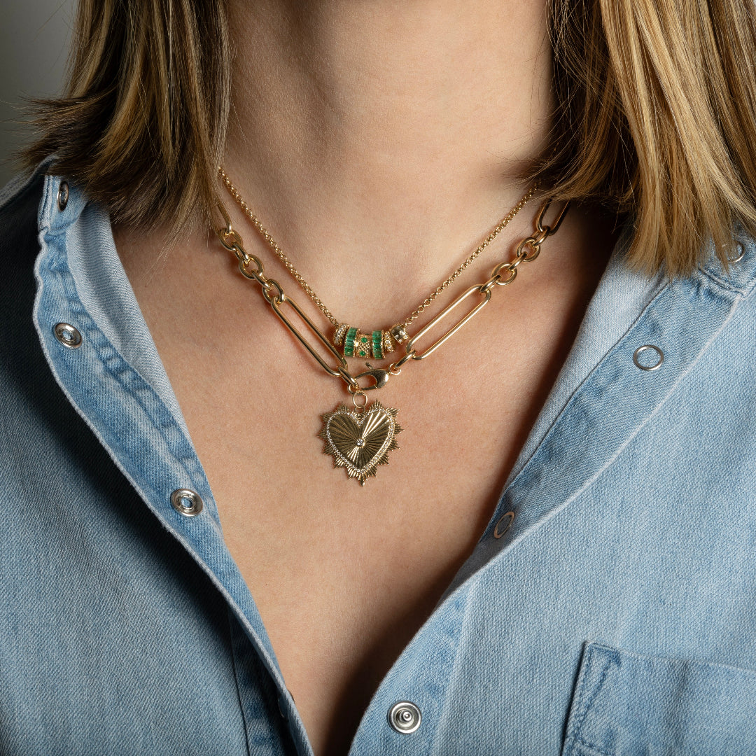 A person wearing two gold chains one with emerald and diamond beads. 