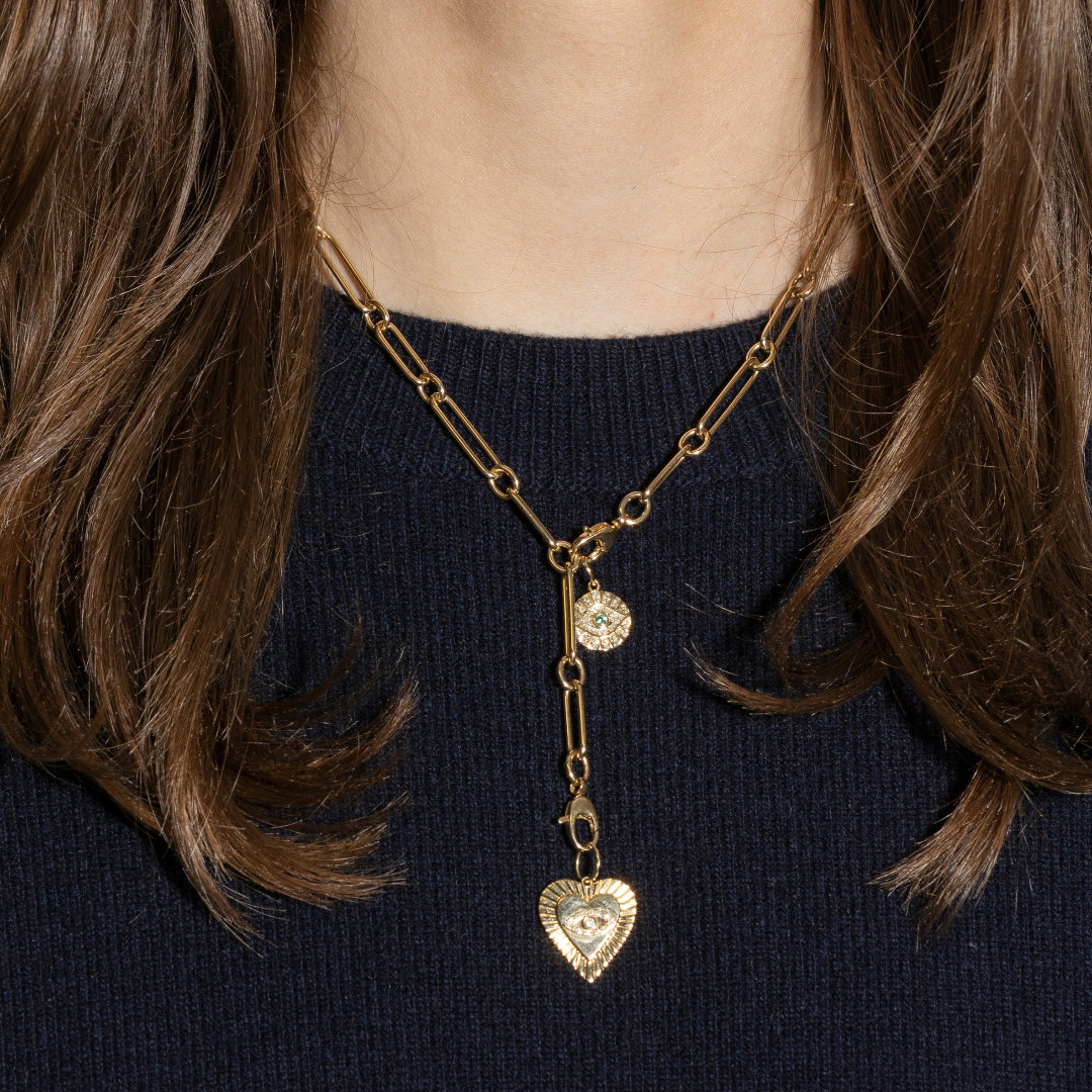 A person wearing a gold necklace with two gold pendants and a black sweater. 