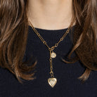 A person wearing a gold necklace with two gold pendants and a black sweater. 