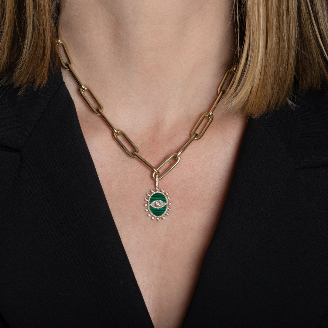 A person wearing a chunky gold paperclip chain necklace with a malachite and diamond evil eye pendant. 