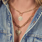 A person wearing two gold paperclip chains. Both chains feature charms attached to the chains with pendant bails. 