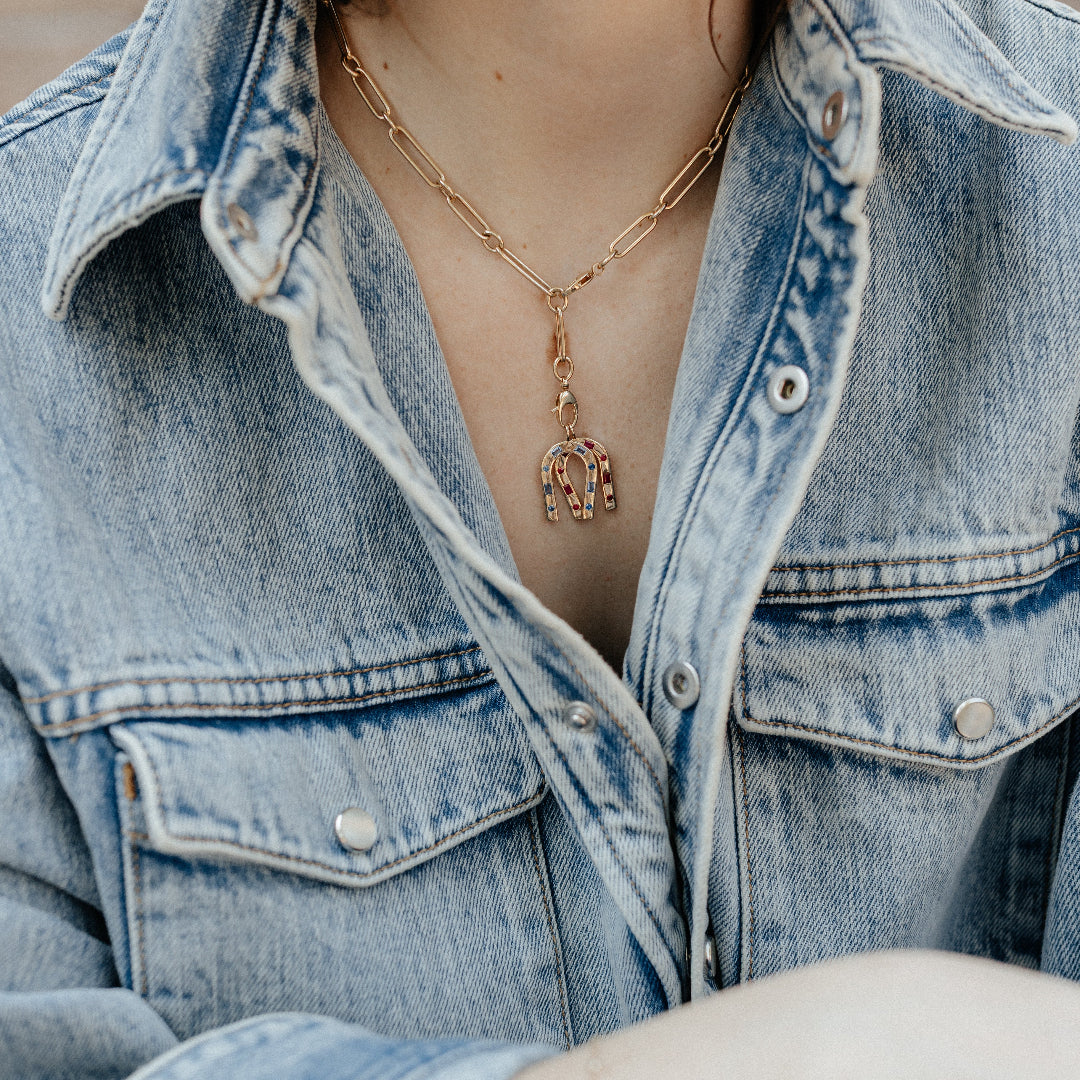 Person wearing a denim jacket with a gold necklace featuring an elephant pendant.