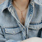 Person wearing a denim jacket with a gold necklace featuring an elephant pendant.