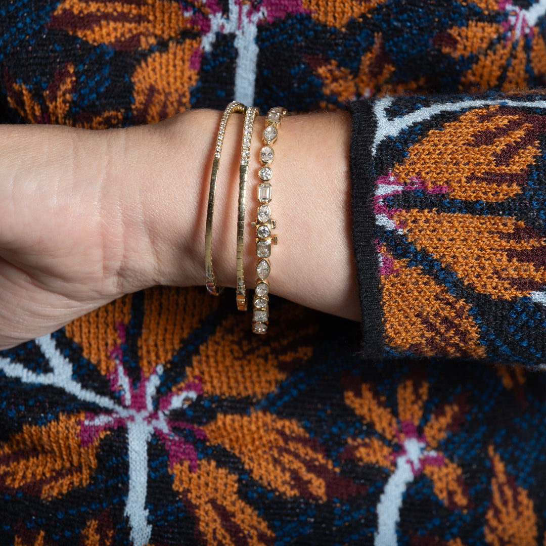 A person wearing three diamond tennis bracelets, showcasing the flexible sides of two of them. 