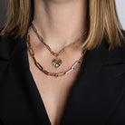 Someone wearing two paperclip chain neckalces, one with a gold heart pendant with diamonds. 