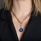 Gold necklace with a blue pendant worn by a person in a black blazer.