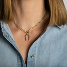 A person wearing a paperclip chain necklace with a Horseshoe Blue Sapphire Pendant attached. 