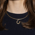 A gold horseshoe pendant on a gold omega chain on a navy blue sweater.