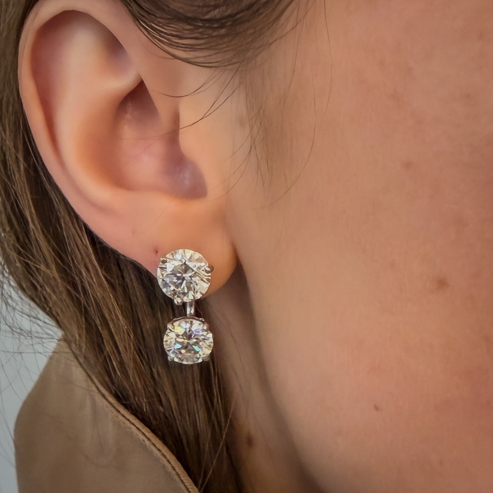 A close-up of a person's ear wearing lab-grown studs and earring jackets, both set in white gold. 