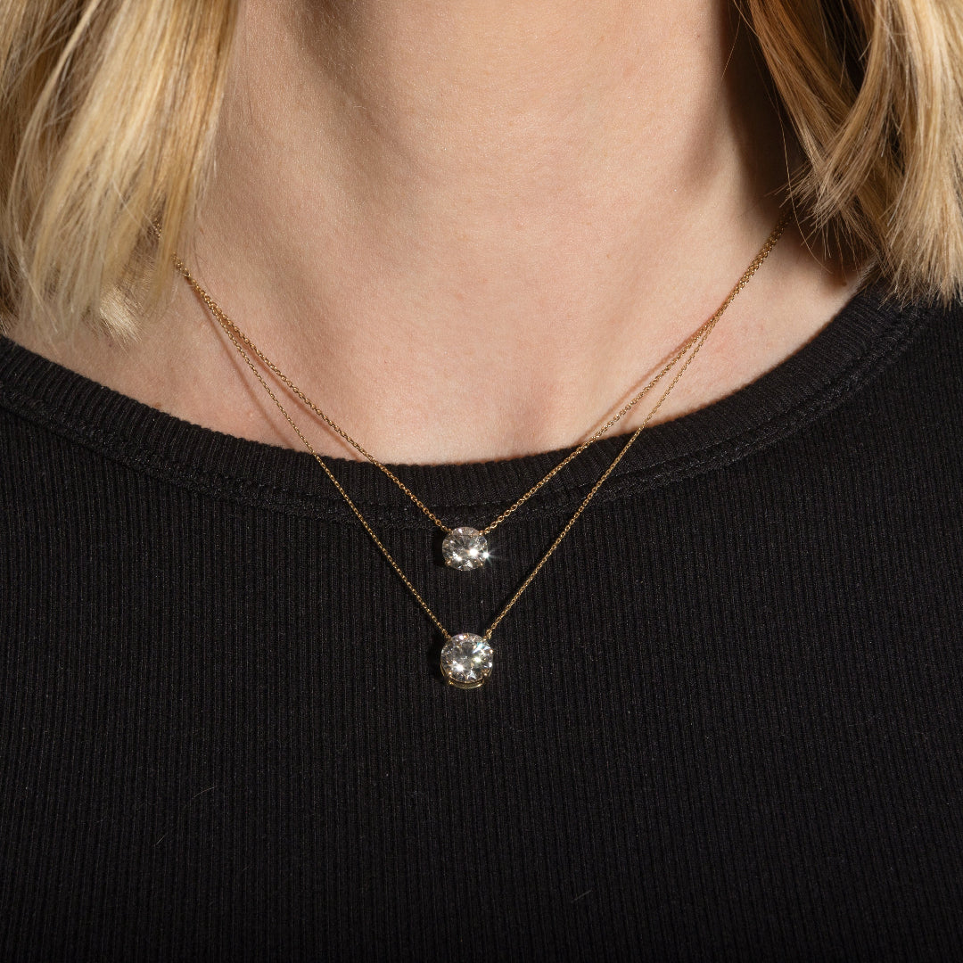Two gold necklaces with solitare lab grown diamonds on a person in a black top.