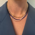 A person wearing two gemstone necklaces made of lapis and rose quarts and a 14k gold paperclip chain. She is also wearing a blue blazer. 