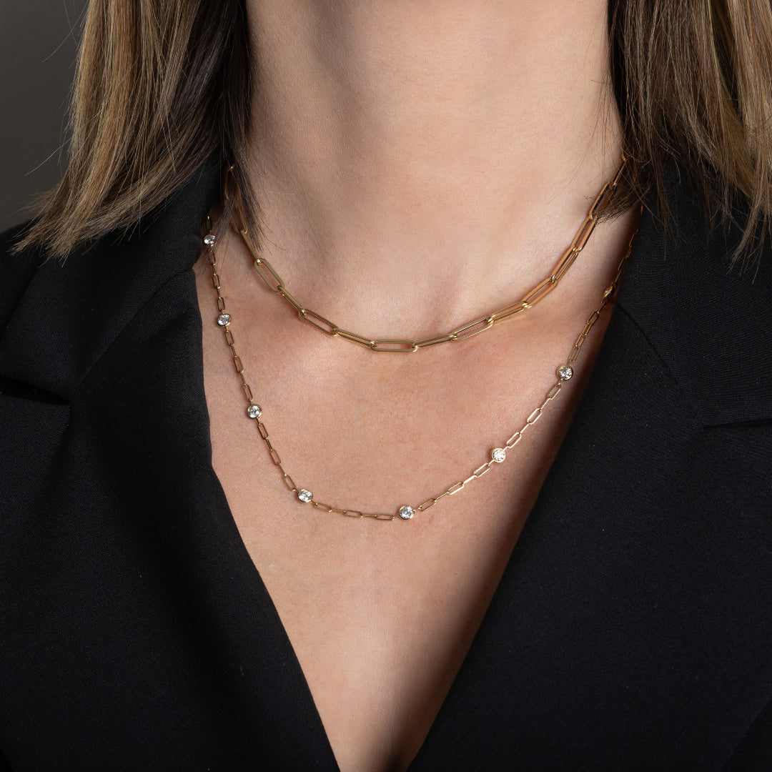 A person wearing two 14k gold chains, one paperclip chain and one diamond station paperclip chain necklace. 
