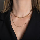A person wearing two 14k gold chains, one paperclip chain and one diamond station paperclip chain necklace. 