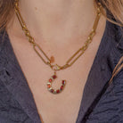 14k gold chain necklace with a horseshoe pendant adorned with garnets worn by a person against a dark background.