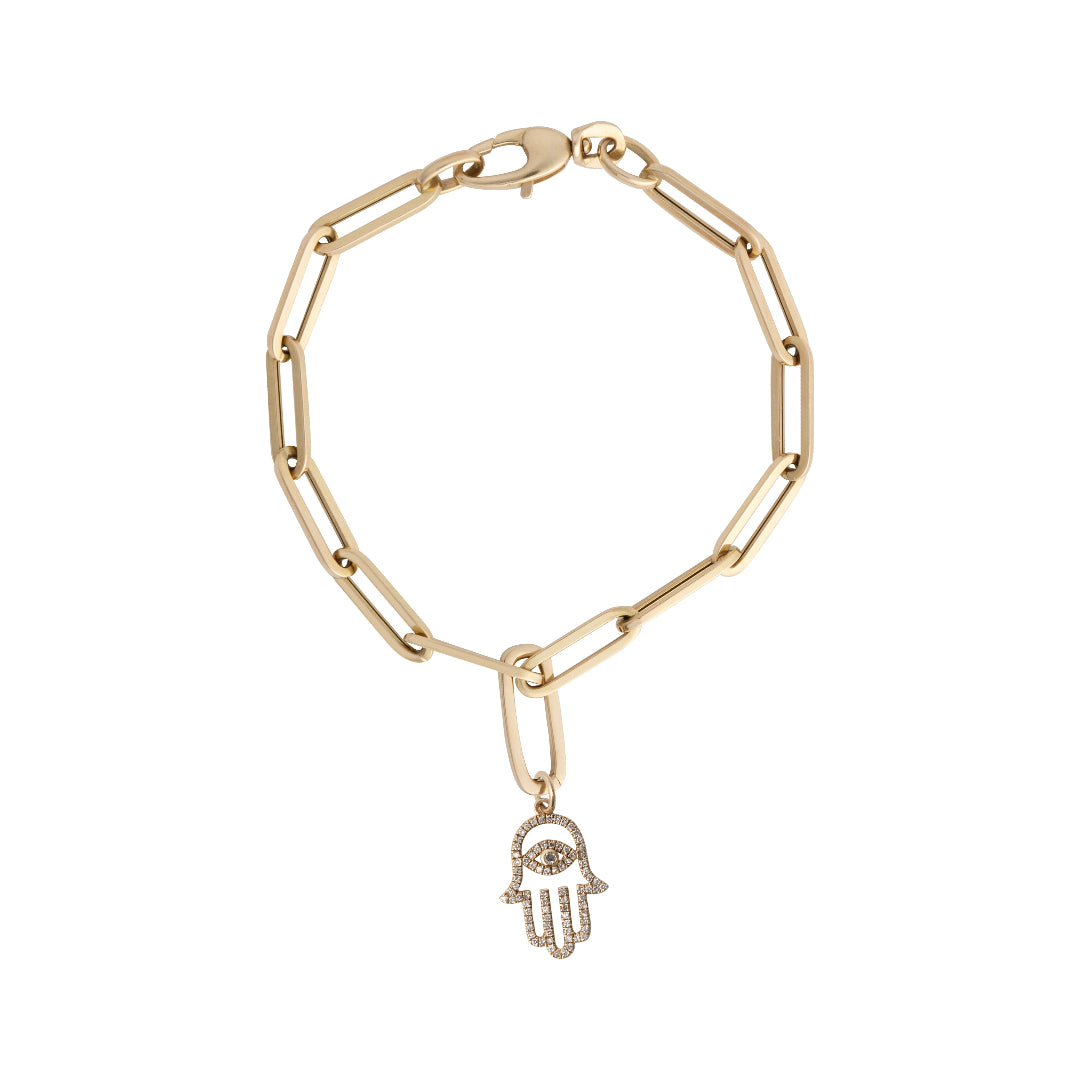 A gold paperclip chain bracelet with a diamond hamsa charm attached with a gold pendant bail laid out on a white background. 